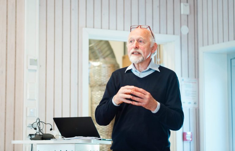 Odd Håpnes står med hendene foran seg. Han har gårtt hår og skjegg, og briller på toppen av hodet. Han er kledd i lyseblå skjorte med en mørk blå genser over. Foto: Thomas Jergel.