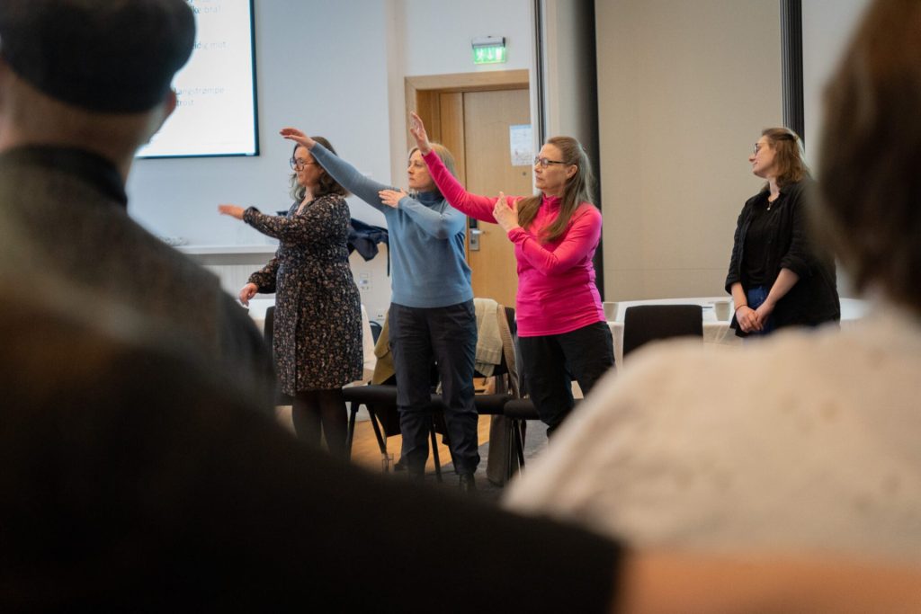 Tre kvinner står med lukkede øyne og beveger armene. I forkant kan vi skimte andre personer. Foto: Alexandra Dahlen.