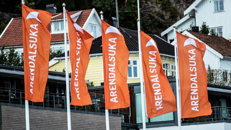 Fem oransje flagg med hvit skrift vaier i vinden. Foto: M. Hauglid.