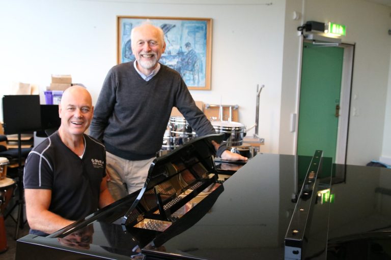 Anders Dalane og Odd Håpnes smiler til kamera. Anders sitter foran et piano og Odd står ved siden av. Anders er kledd i mørk t-skjorte. Odd har grått hår og skjegg, og er kledd i mørk genser og lys bukse. Foto: Marthe Haugdal.