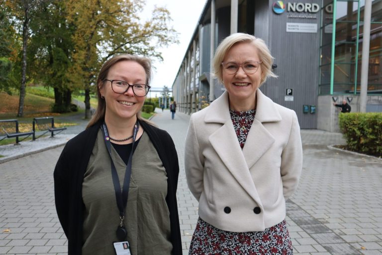 Marit Stranden og Ingvild Kjerkol står ved siden av hverandre utenfor Nord universitet. De smiler til kamera. Foto: Marthe Haugdal.