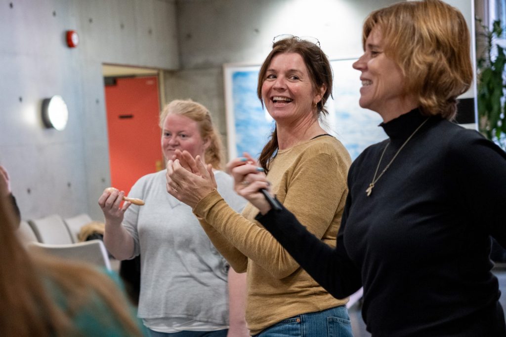 Grete Daling står sammen med to andre kvinner. Hun smiler og klapper i hendene. Foto.