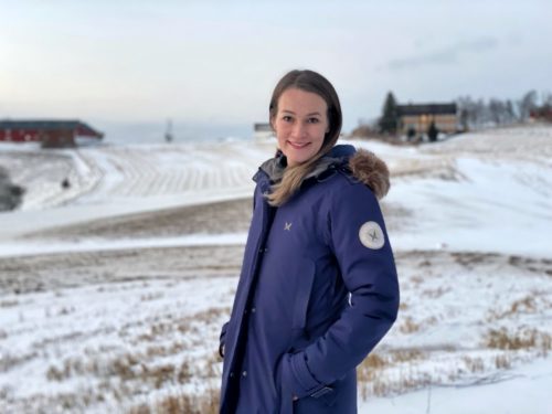 Alexandra Dahlen står ute i et vinterkledd landskap. Det er hvitt på bakken. Hun har på seg en blå vinterkåpe.