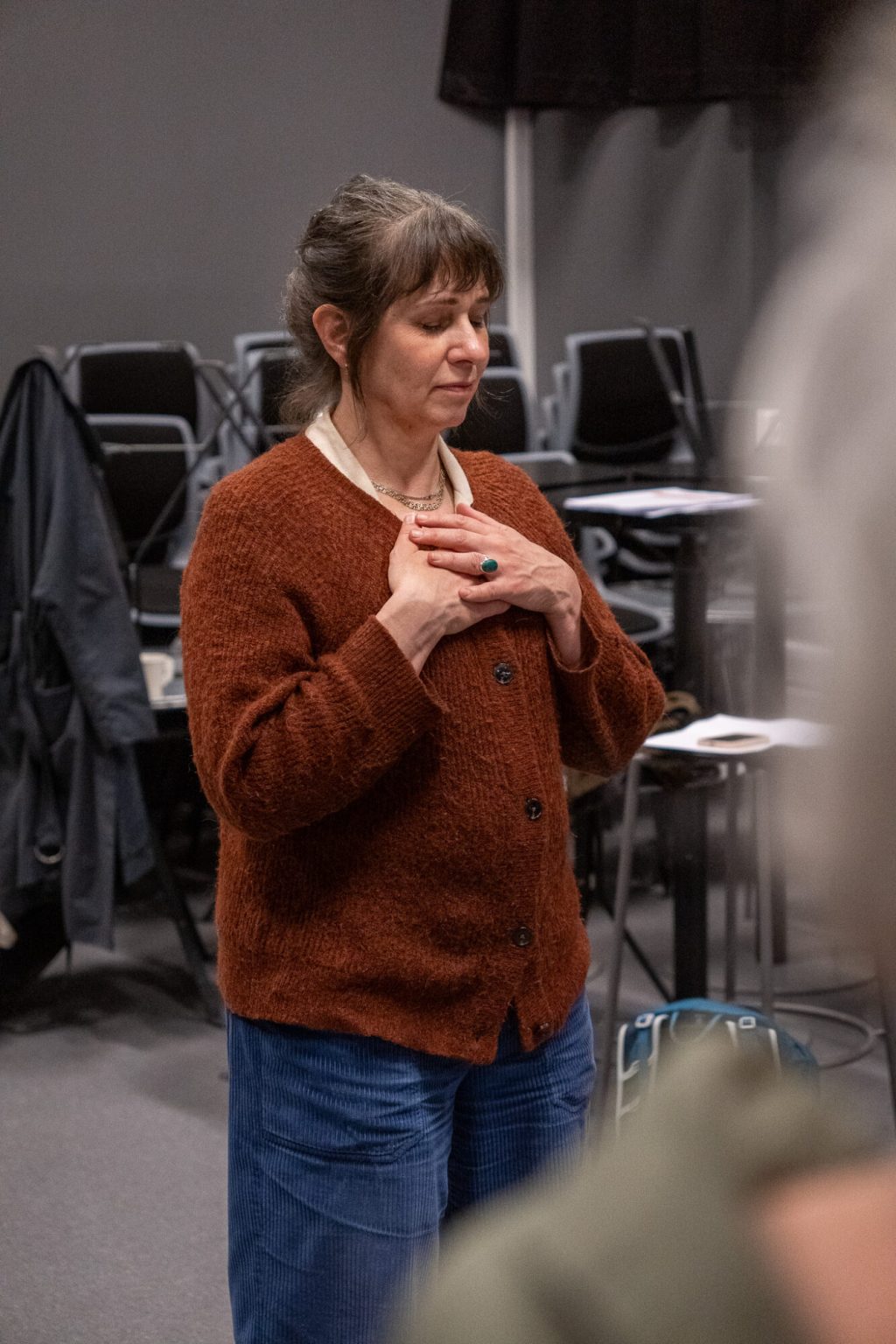 Anna Nordansted står med hendene på brystet. Hun har lukkede øyne. Hun er kledd i en blå bukse, rustrød cardigan og har håret oppsatt. Foto: Alexandra Dahlen.