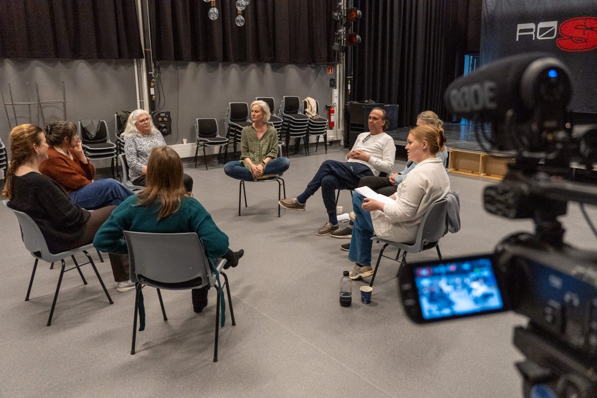 8 personer sitter på stoler i en en ring. Til høyre i bildet kan vi skimte et videokamera. Foto: Alexandra Dahlen.