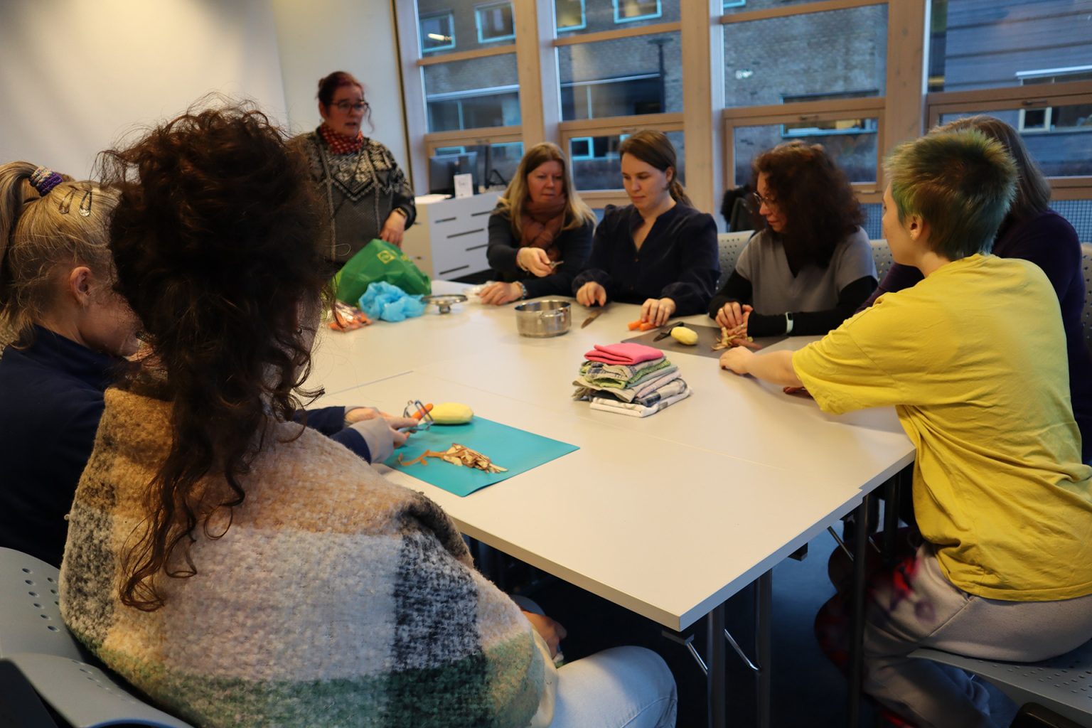 En gruppe studenter sitter sammen rundt et bord. De skreller poteter og gulerøtter. Foto: Marit Stranden.