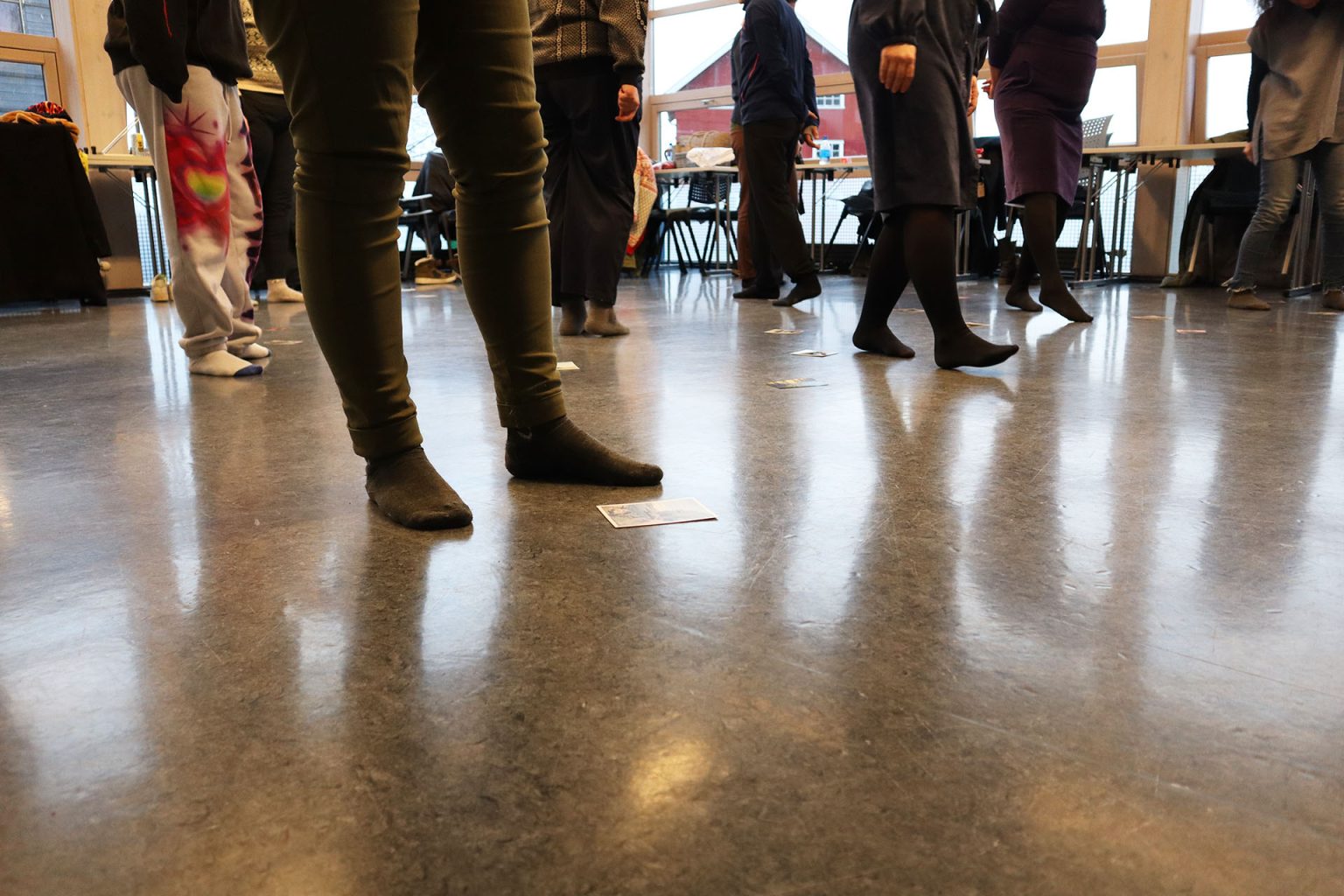 Flere personer går rundt på gulvet i sokkelesten. Det ligger også ulike kort på gulvet. Foto: Marit Stranden.