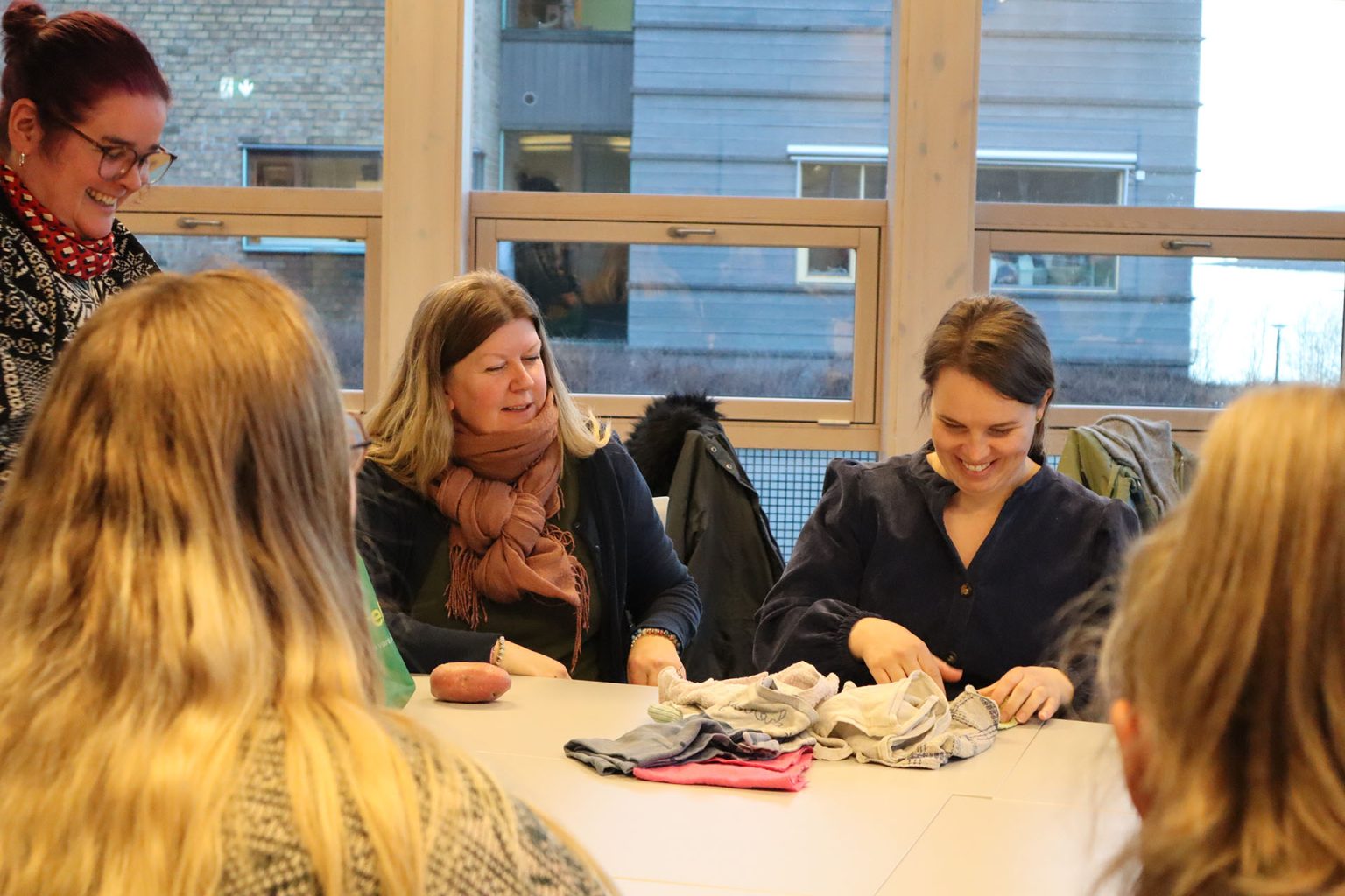 Noen studenter fra videreutdanningen "Kunst og kultur i helse og omsorg" sitter sammen ved et bord. På bordet ligger noen kluter. Studentene smiler. Foto: Marit Stranden.