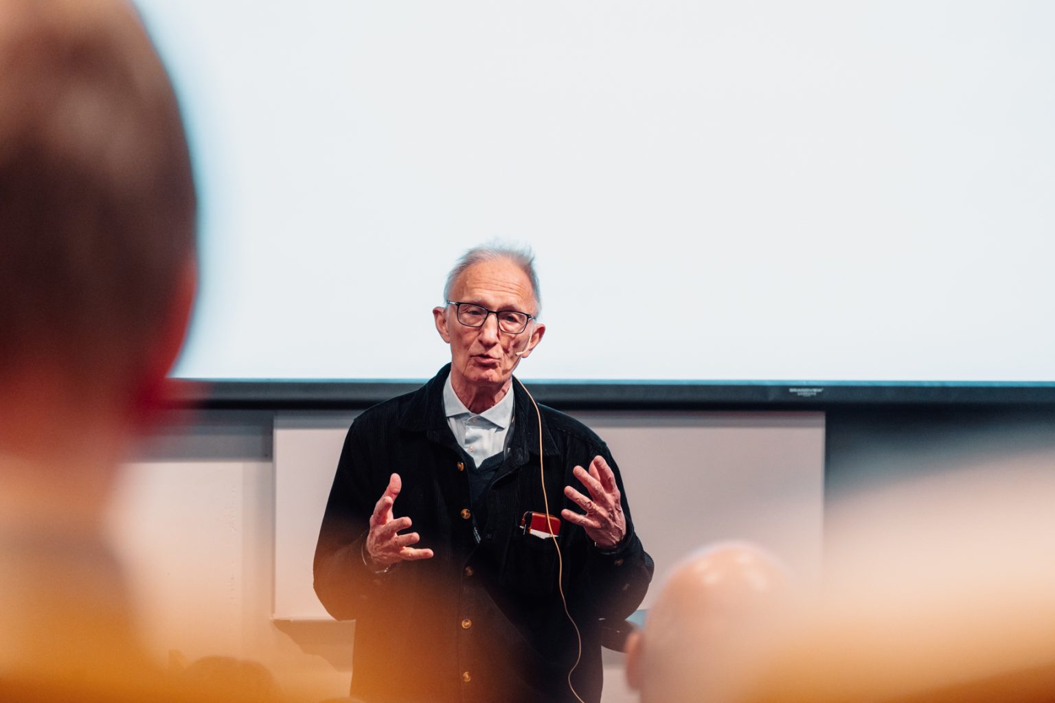 Töres Theorell holder foredrag. Han har kort, grått hår og briller. Han har på seg en lys skjorte og en mørk jakke over. Foto: Christian Trustrup, TA-Kreativ.