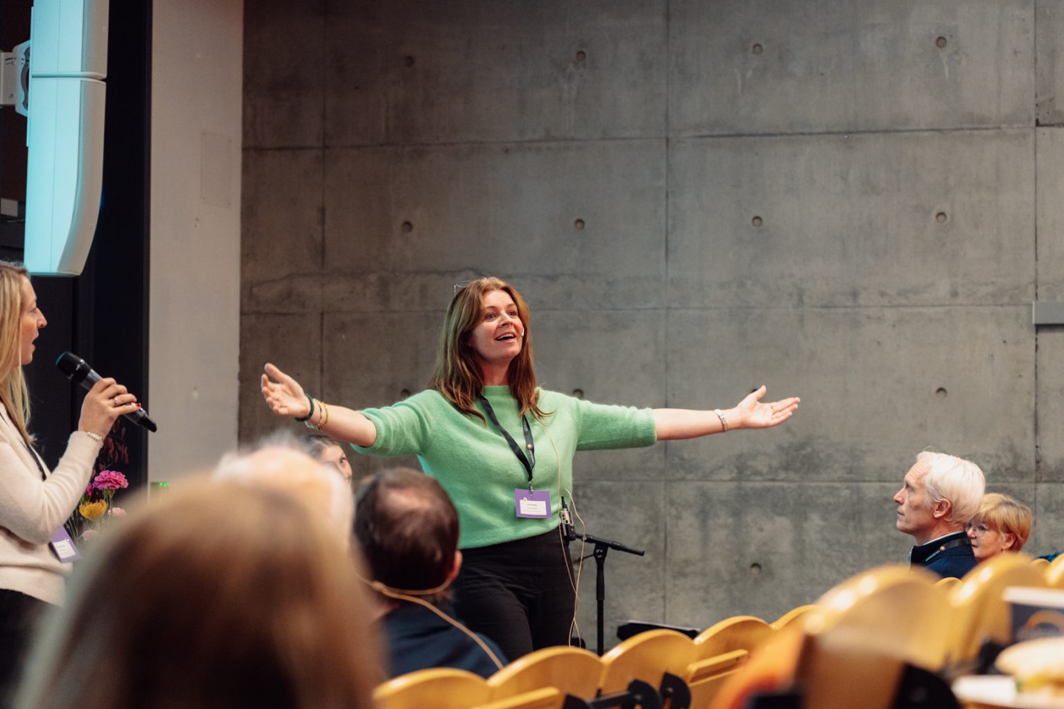 Grete Daling er emneansvarlig for videreutdanningen "Musikkbasert miljøbehandling" ved Nord universitet. Hun har langt, mørkt hår, grønn genser, sort bukse. Hun strekker hendene ut mens huns synger i en forelesningssal. Foto: Christian Trustrup, TA-Kreativ.