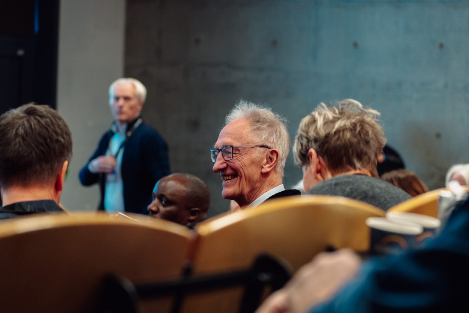 Töres Theorell sitter i en forelesningssal sammen med andre. Han har kort, grått hår og briller. Han smiler. Foto: Christian Trustrup, TA-Kreativ.