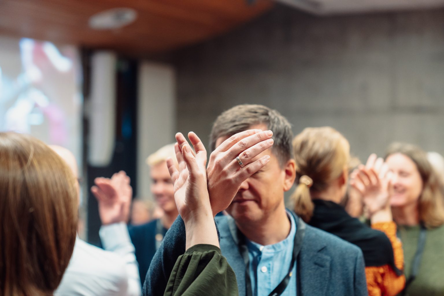 En mann står med sin høyre hånd ut og lener den mot en annen person sin hånd. I bakgrunnen ser vi flere personer i en forelesningssal. Foto: Christian Trustrup, TA-Kreativ.