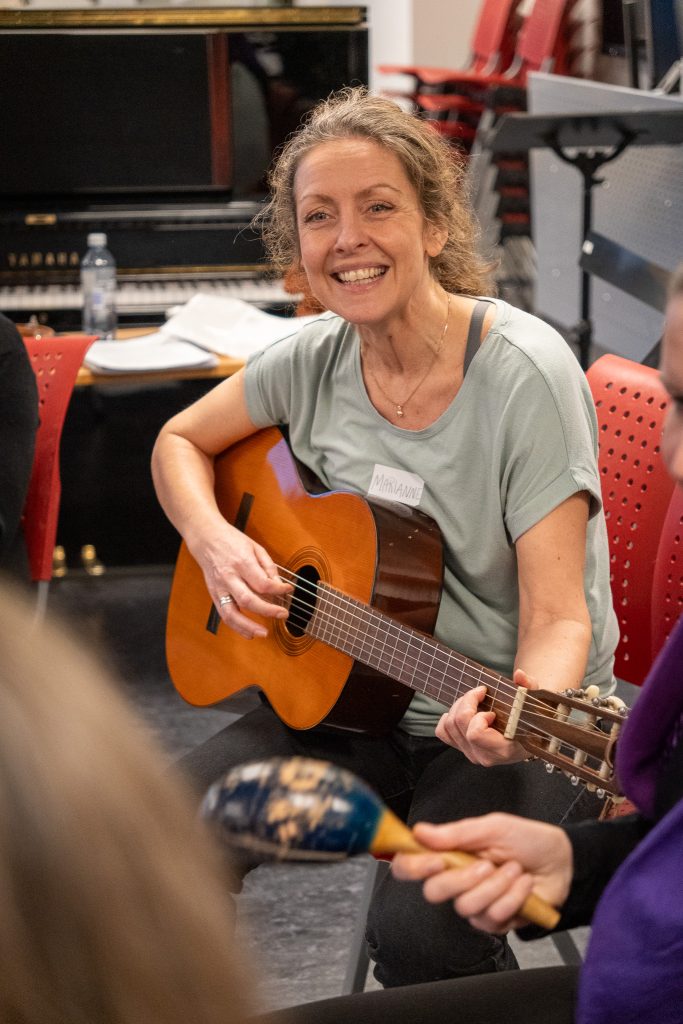 En kvinne sitter og spiller gitar. Hun har hestehale, grønn t-skjorte og sort bukse. Foto: Alexandra Dahlen.