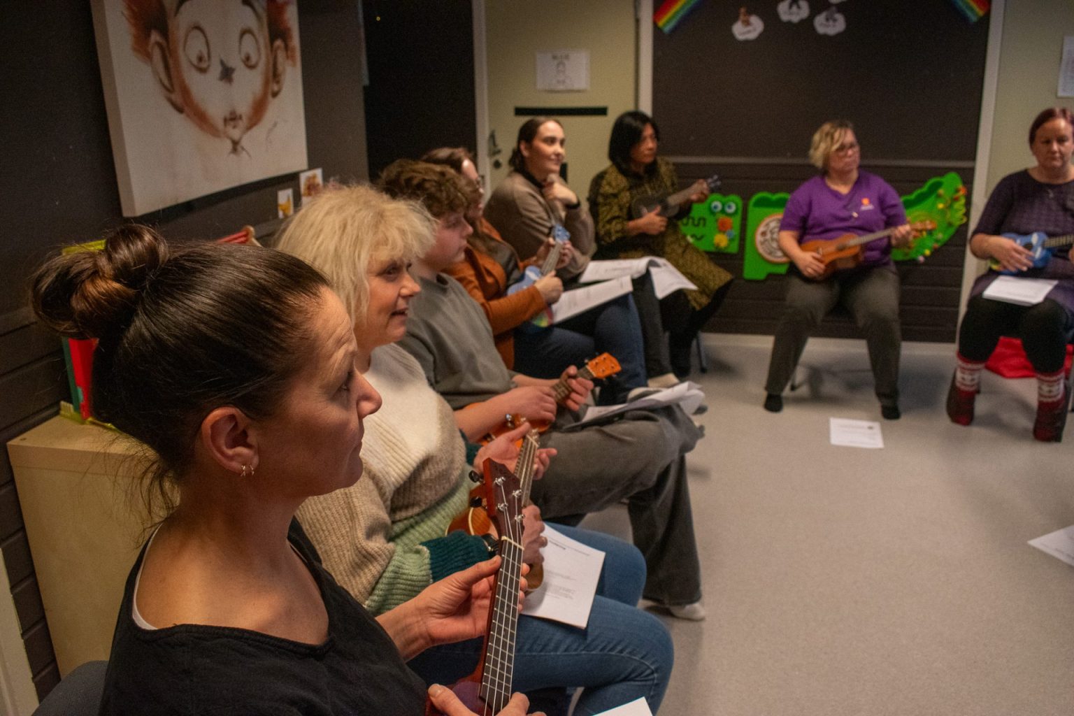 Flere voksne sitter på rad og spiller ukulele. Foto.