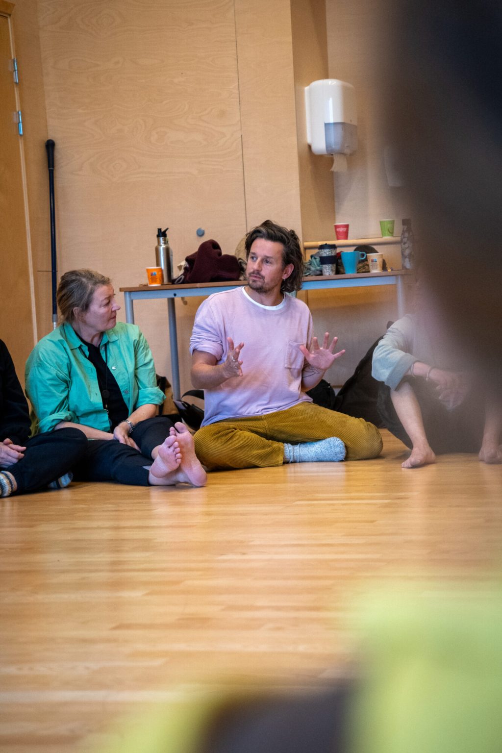 Siri Wigdel og Cai Tomos sitter på gulvet sammen med andre mennesker. Foto.