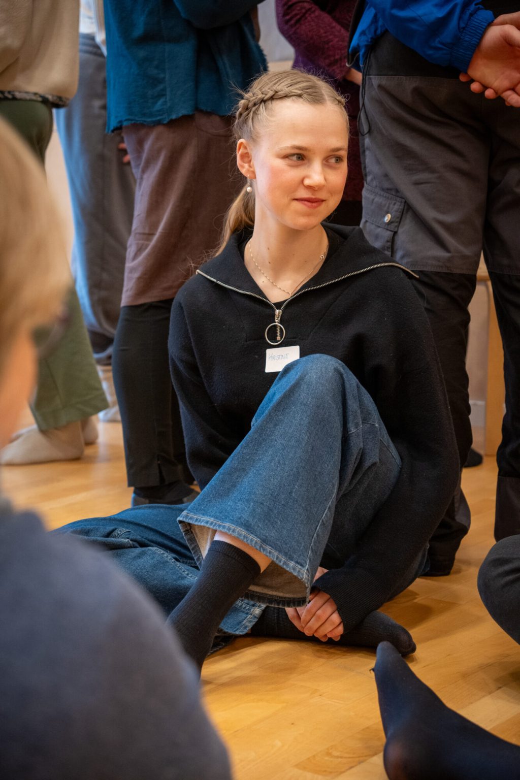 En ung kvinne sitter sammen med andre på gulvet. Foto.