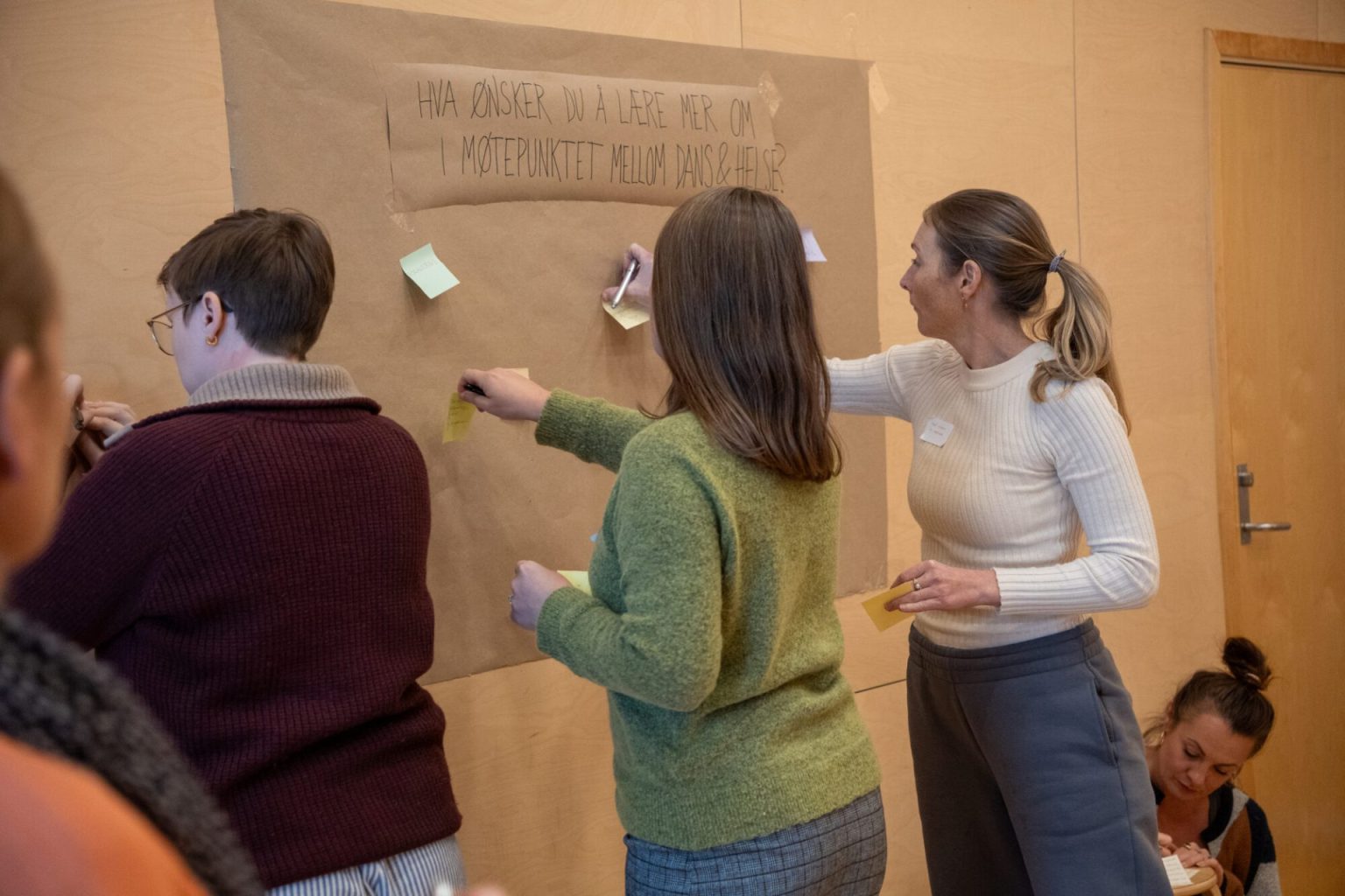 Tre personer henger opp post it lapper på en vegg. Foto.