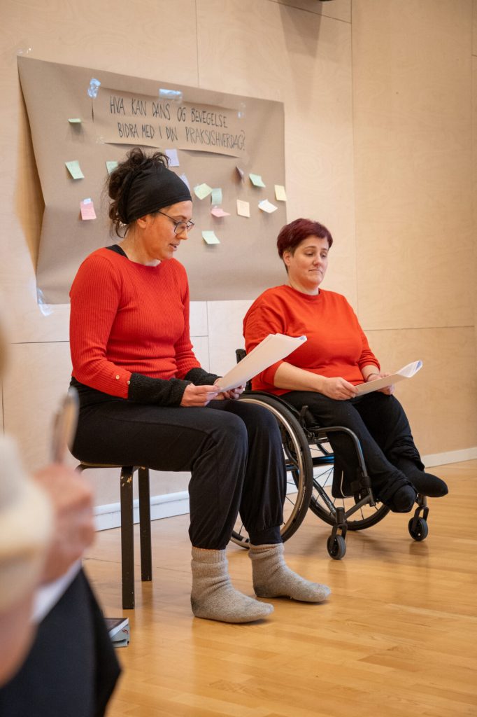 Tone Pernille Østern og Elen Øyen sitter ved siden av hverandre. Begge er kledd i rød topp og sort bukse. Bildet er tatt under danseseminaret "Å skape meningsfulle dager". Foto: Alexandra Dahlen.