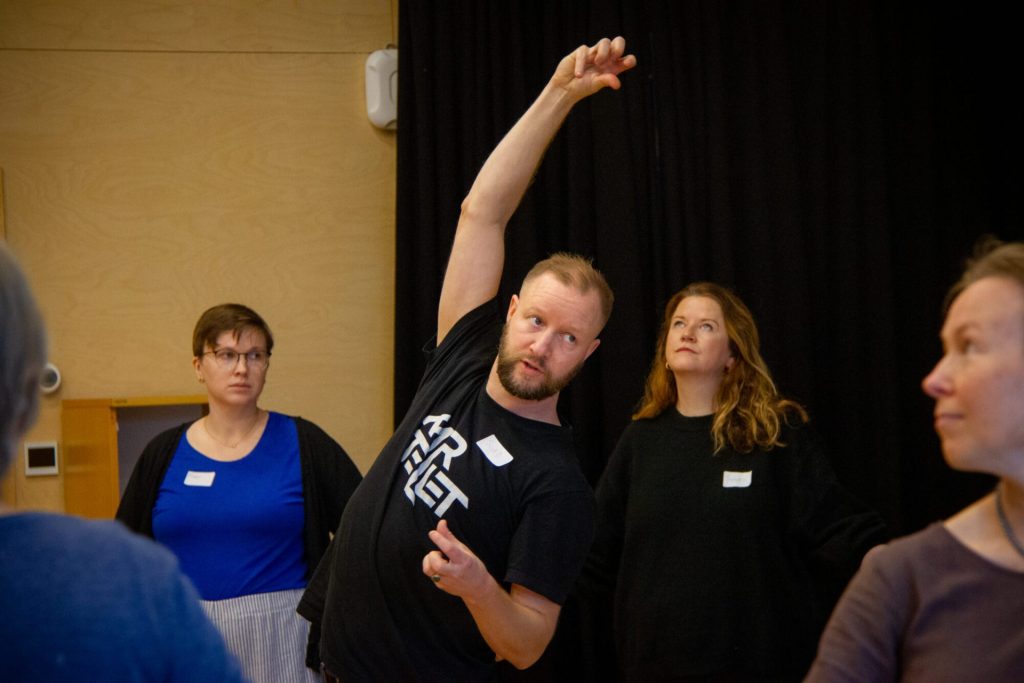 Sigurd Johan Heide viser frem ulike danseøvelser. Han var en av instruktørene under danseseminaret "Å skape meningsfulle dager". Rundt ham ser vi flere kvinner som følger med på Sigurd sine forklaringer. Foto: Alexandra Dahlen.