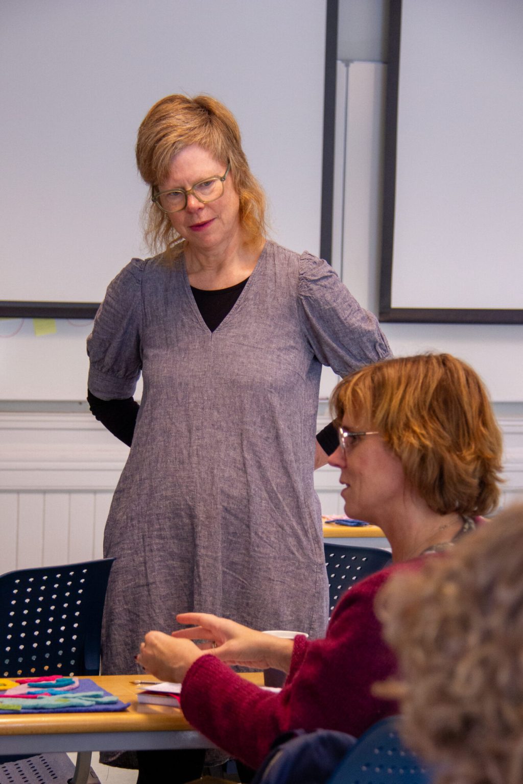 Anne Helga Henning står og snakker med en student som sitter ved pulten. Foto.