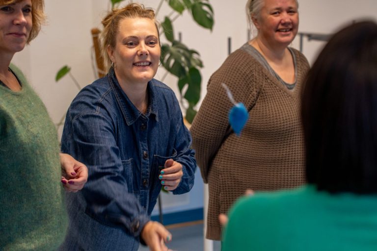 En kvinne kaster en blå ertepose til en annen kvinne. Hun smiler. Hun har håret oppsatt og er kledd i en blå skjorte. Rundt henne står andre kvinner. Foto: Alexandra Dahlen.