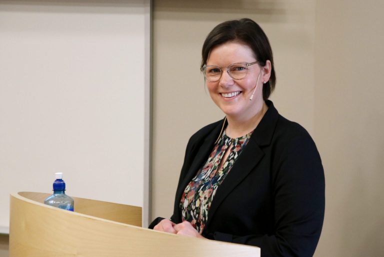 Bente Irene Løkken står ved et talerbord og smiler til kamera. Foto: Alexandra Dahlen.