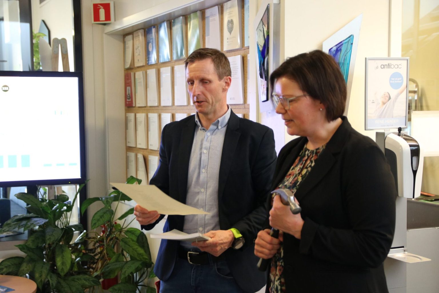 Vegar Rangul og Bente Irene Løkken står ved siden av hverandre. Vegar holder i doktorgradsavhandlingen. Bente holder en hammer. Foto: Alexandra Dahlen.