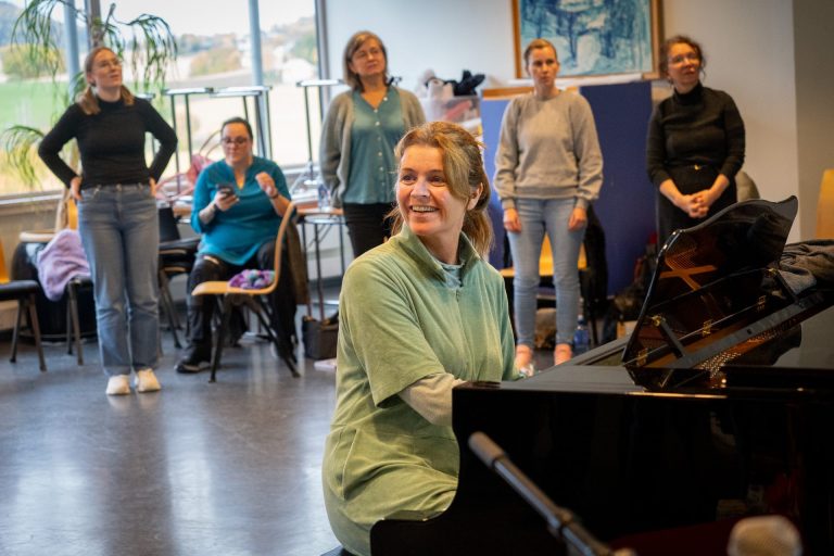 Grete Daling sitter ved et piano og bak henne står studentene og synger.