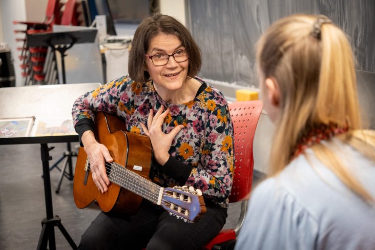 En kvinne sitter med en gitar i fanget og smiler.