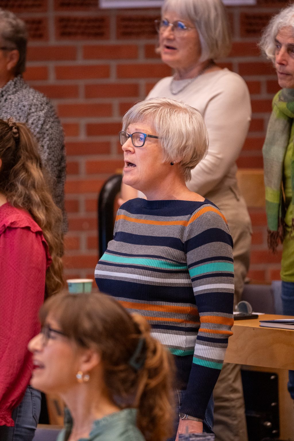 En kvinne står sammen med andre i et auditorium og synger.