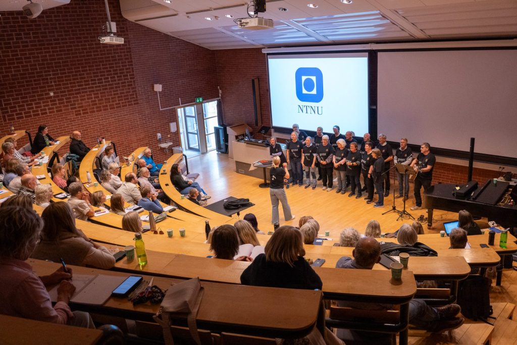 Gnist demenskor står foran i et auditorum og synger.