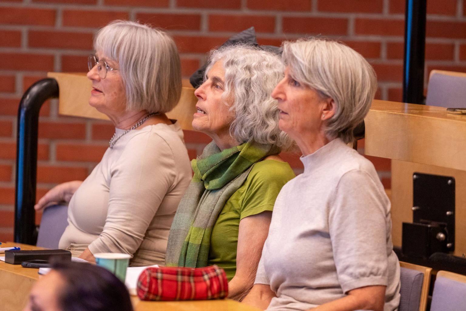 Tre kvinner sitter sammen i et auditorium.