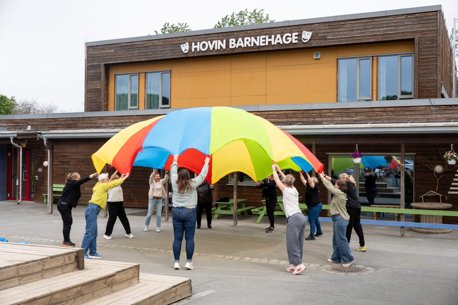 Ansatte i Hovin barnehage holder fast i en fallskjerm som de løfter opp.