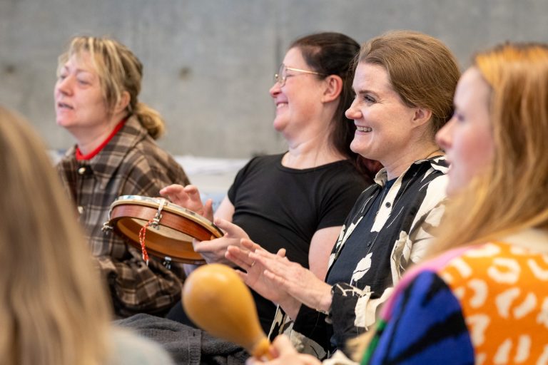 Flere kvinner sitter sammen og spiller på rytmeinstrument.
