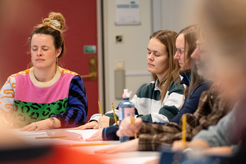 Fire kvinner sitter sammen og tegner med lukkede øyne.