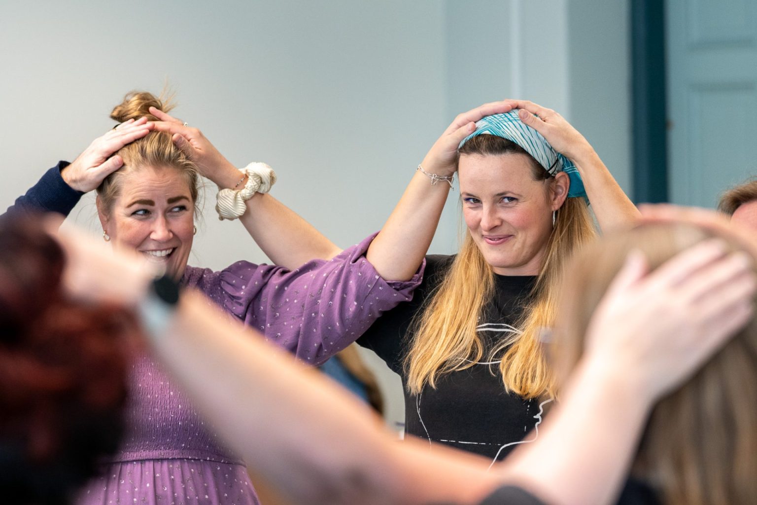 To kvinner står i en sirkel med andre. De smiler og holder hendene på hodet til hverandre.