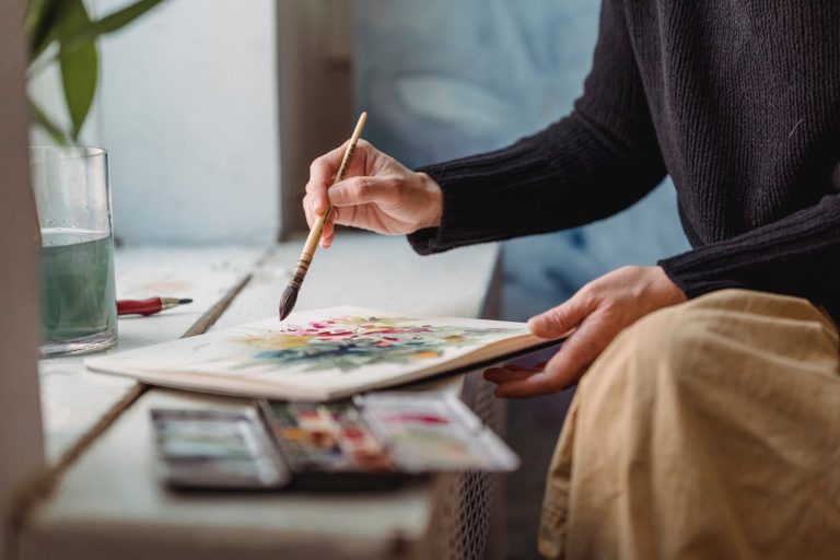 Illustrasjonsbilde: En persone sitter ved en vinduskarm og maler på ark.