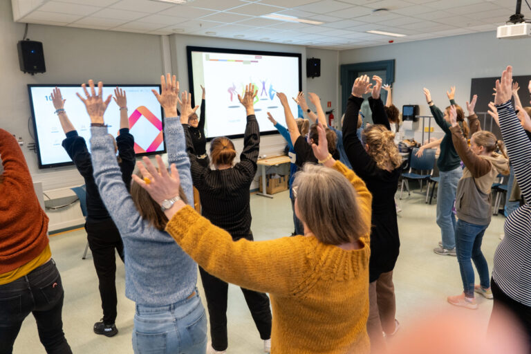 Ragnhild Skille står foran en gruppe med studenter. Alle strekker hendene over hodet.